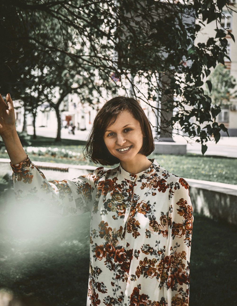 woman in white and brown floral long sleeve shirt standing near tree during daytime