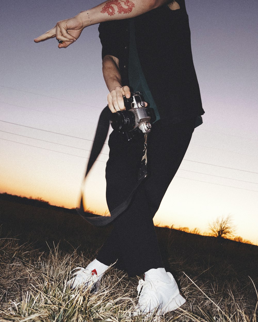 person in black pants and white sneakers standing on grass field during sunset