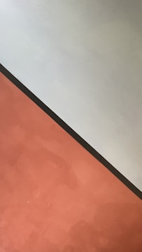 A minimalist composition featuring two distinct color blocks divided diagonally. The upper section is light gray, while the lower section is a muted terracotta. A thin, dark line separates the two colors, creating a stark contrast.