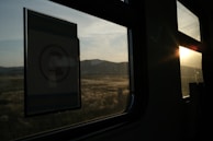 Sunset over a quiet village seen from a train window with silhouettes of passengers.