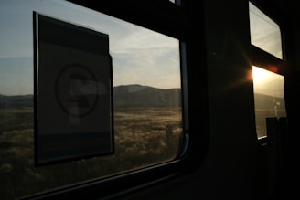 Sunset over a quiet village seen from a train window with silhouettes of passengers.