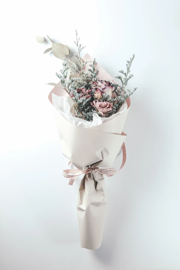 A slim bouquet of dusty pink flowers and silvery greenery wrapped in white paper with a bow