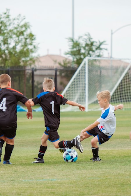 Trois enfants jouant au football sur un terrain en herbe, l'activité phare des stages sportifs du congé d'automne 2026