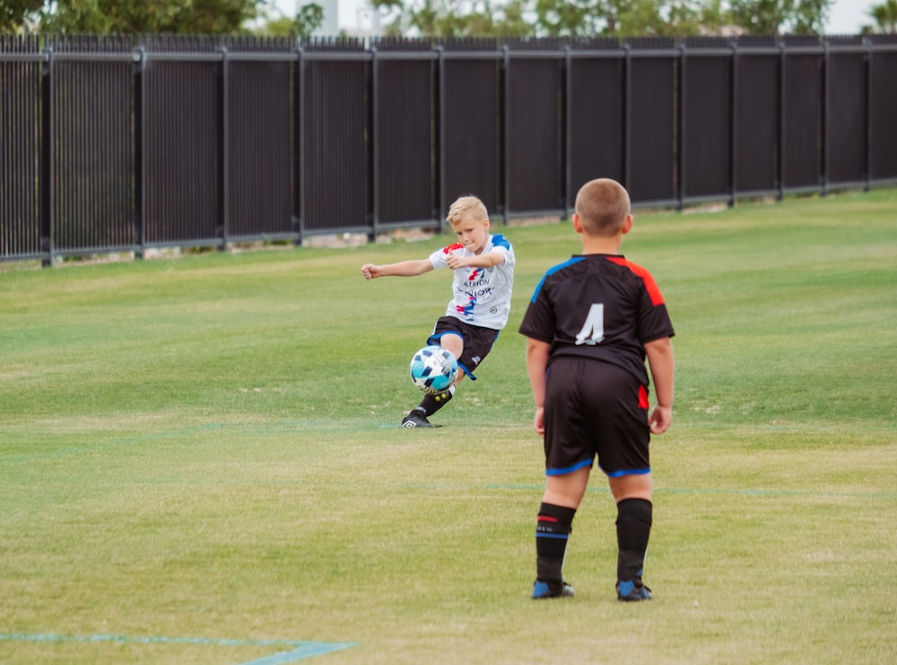 昼間、緑の芝生のグラウンドでサッカーをする2人の男の子