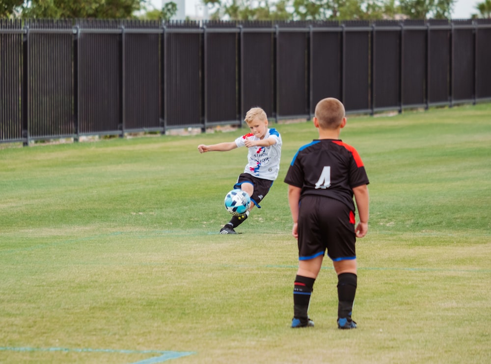 2 boys playing soccer on green grass field during daytime