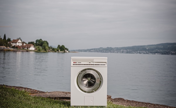 white front load washing machine on green grass field near body of water during daytime