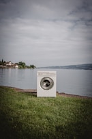 white front load washing machine on green grass field near body of water during daytime