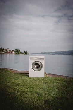 white front load washing machine on green grass field near body of water during daytime