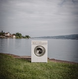 white front load washing machine on green grass field near body of water during daytime