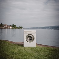 white front load washing machine on green grass field near body of water during daytime