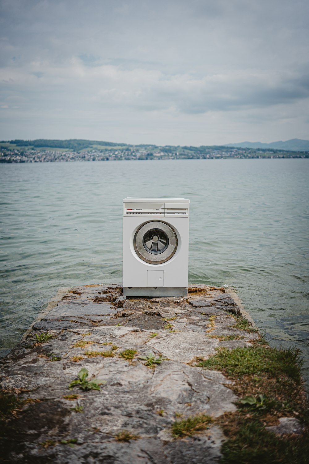 white front load washing machine on brown rock near body of water during daytime