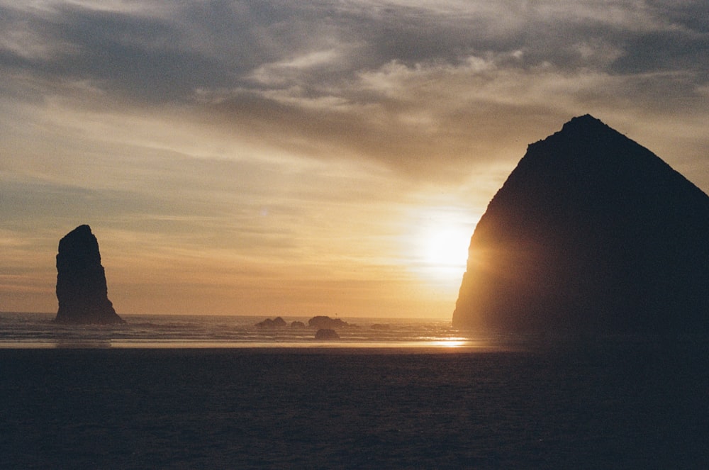 silhouette of rock formation near body of water during sunset