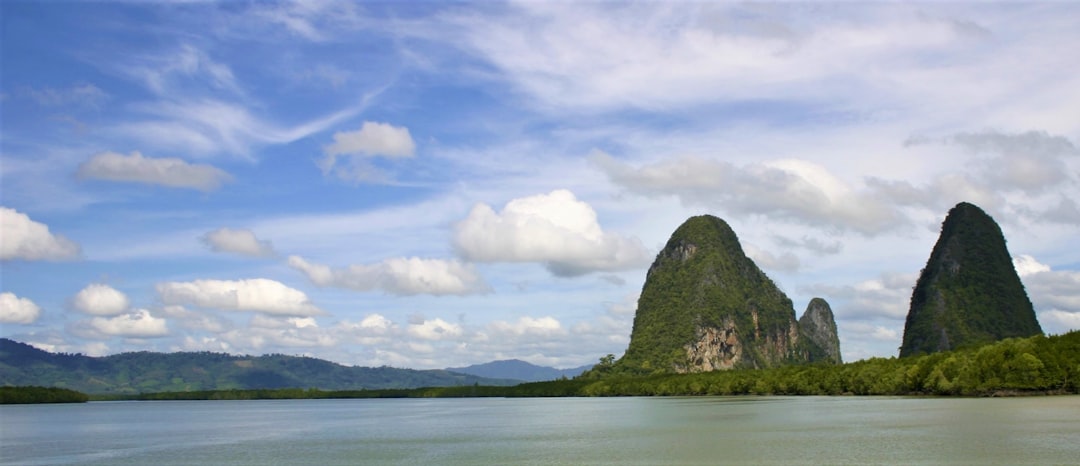green and brown mountain beside body of water under white clouds and blue sky during daytime