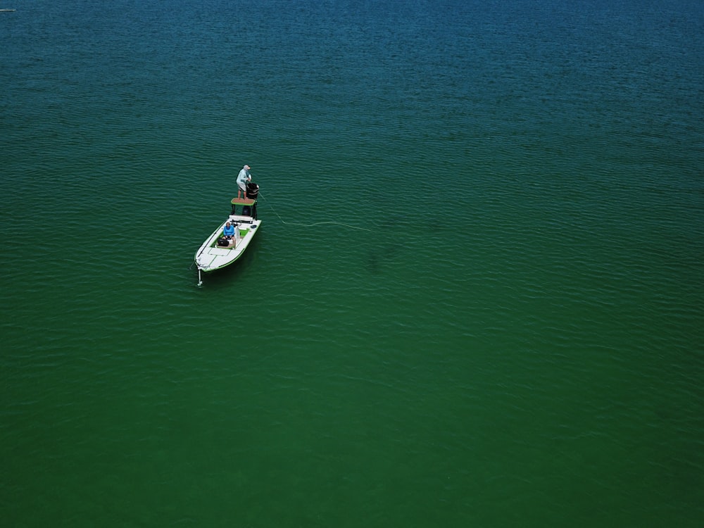 man in white and red shirt riding white and blue boat on green sea during daytime