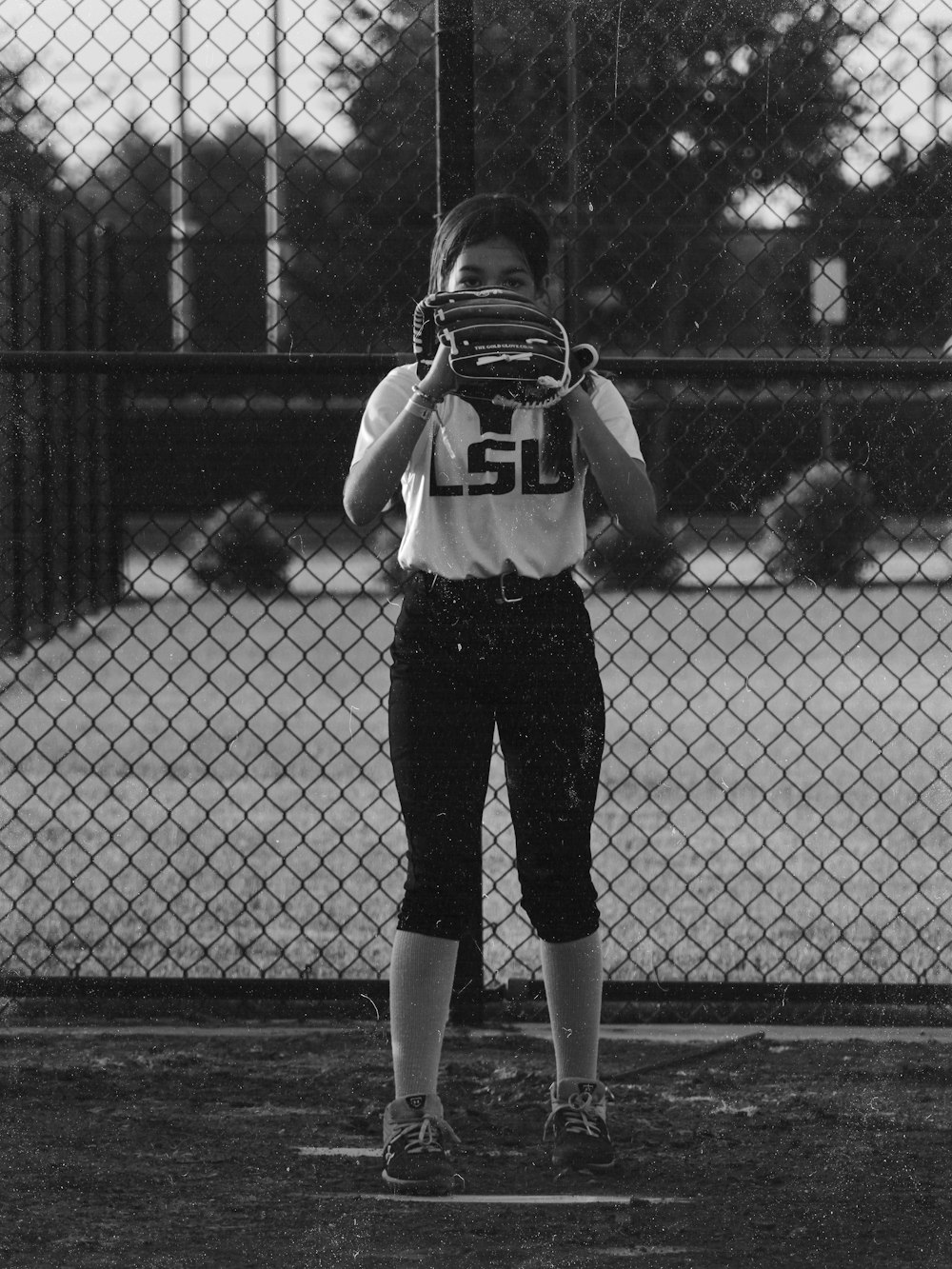 grayscale photo of woman in white shirt and black pants standing beside fence