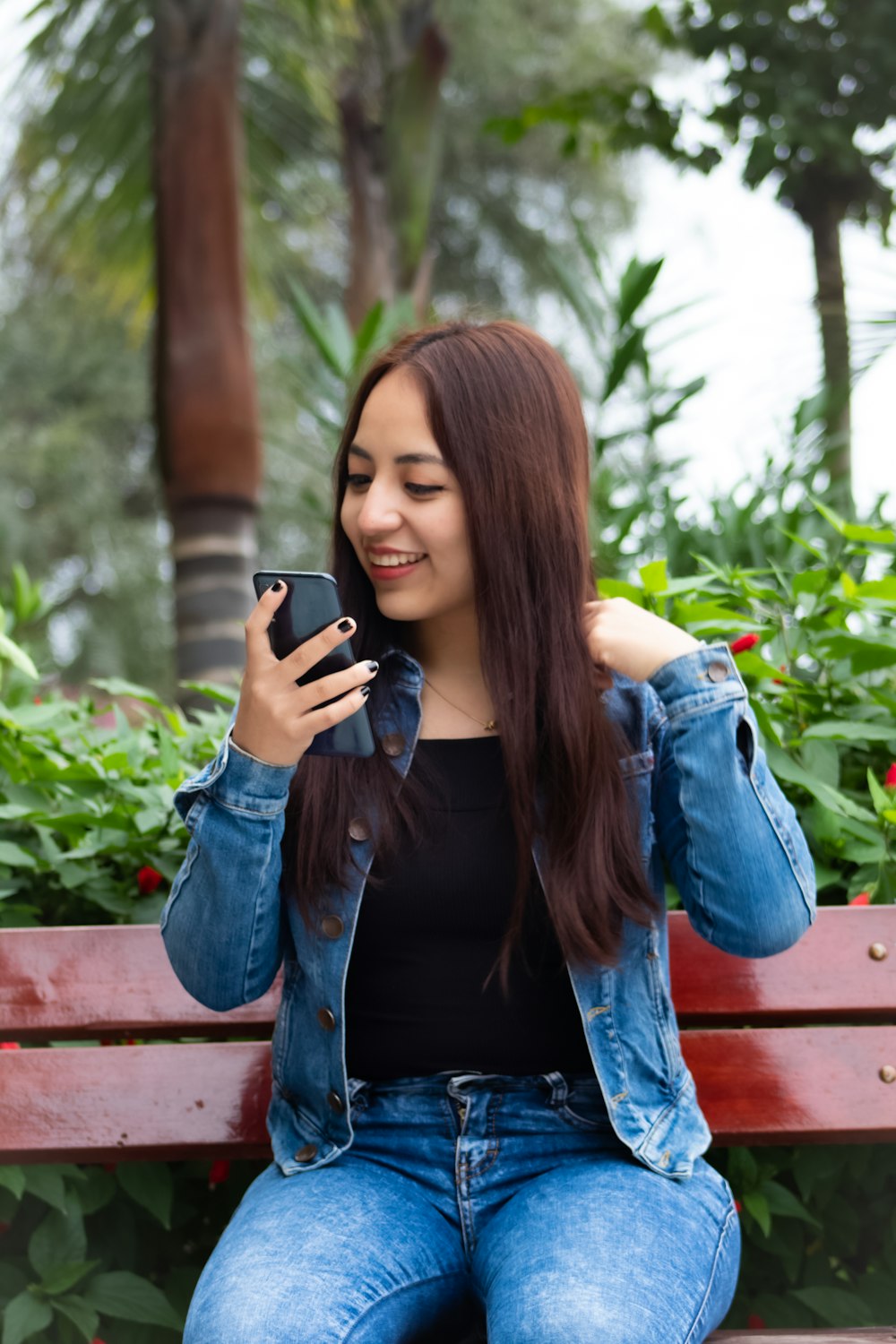 woman in black leather jacket and blue denim jeans sitting on brown wooden bench