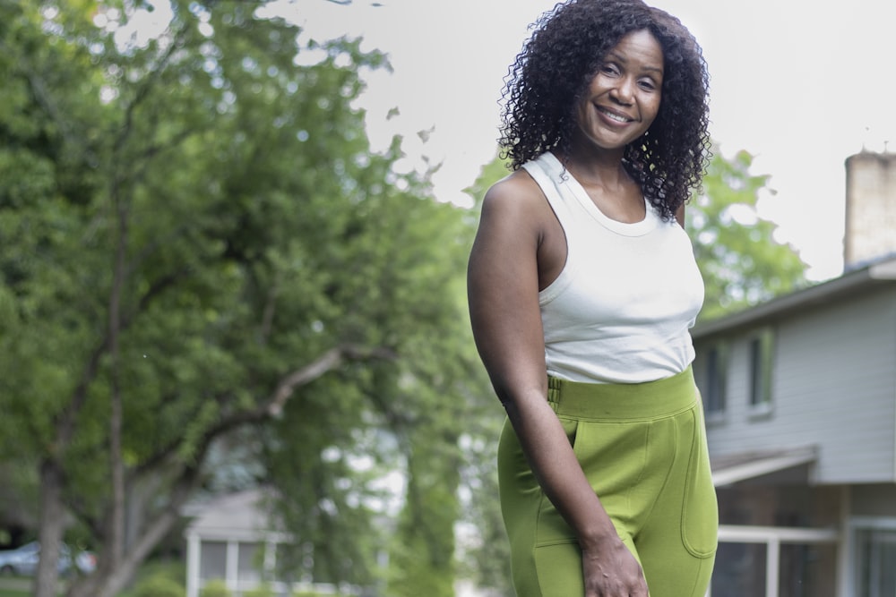 woman in white tank top and green shorts standing near green trees during daytime