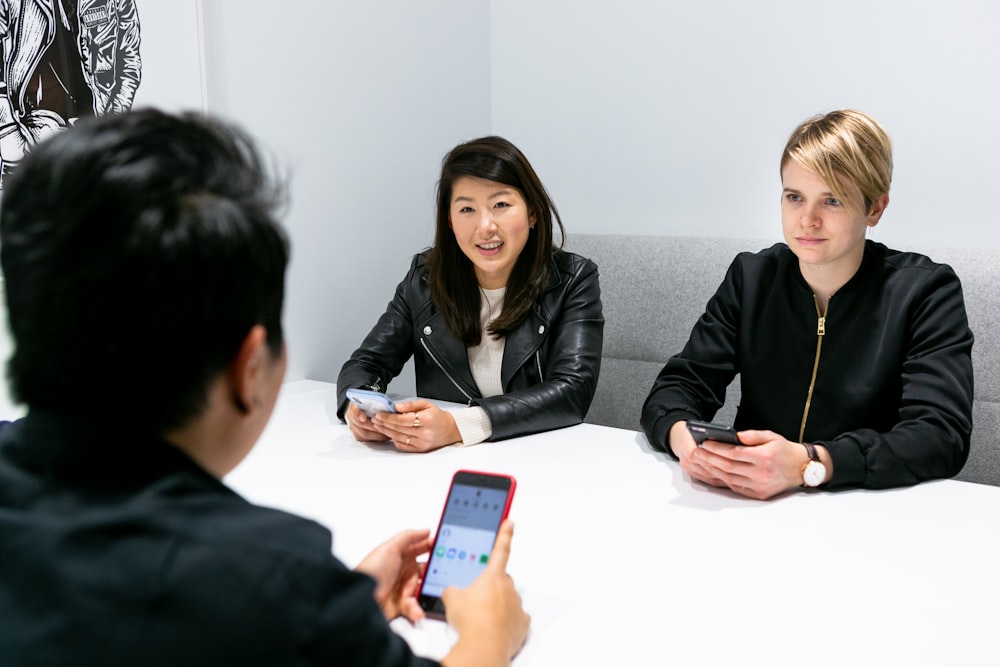 three people in a meeting wearing black jacket holding phones