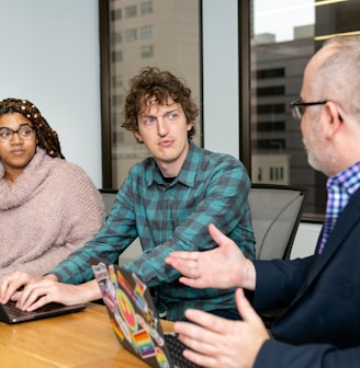 three people, one woman and two men, on laptops in a boardroom