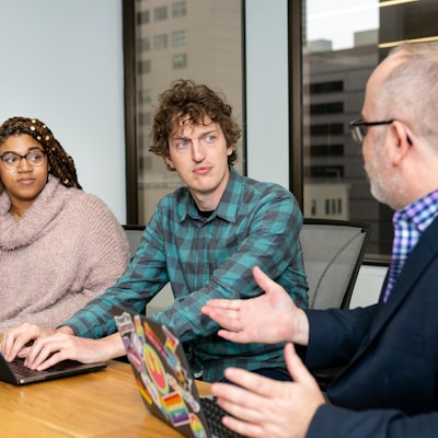 three people, one woman and two men, on laptops in a boardroom