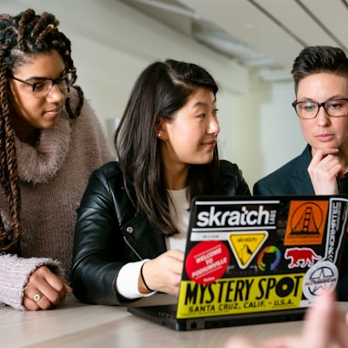 three people around a laptop with stickers on it