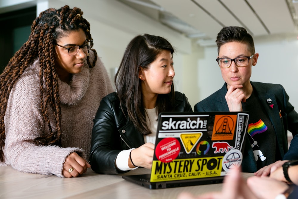 three people around a laptop with stickers on it