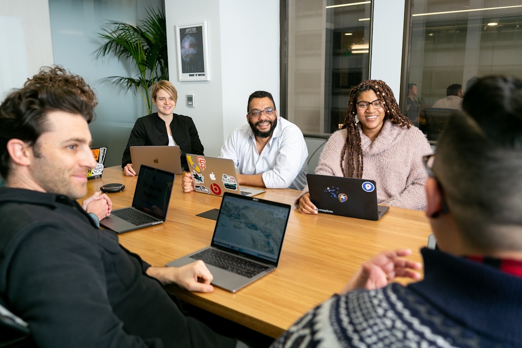 meeting cadence: four people all on laptops, two men and two women, listen to person talking in a board meeting 