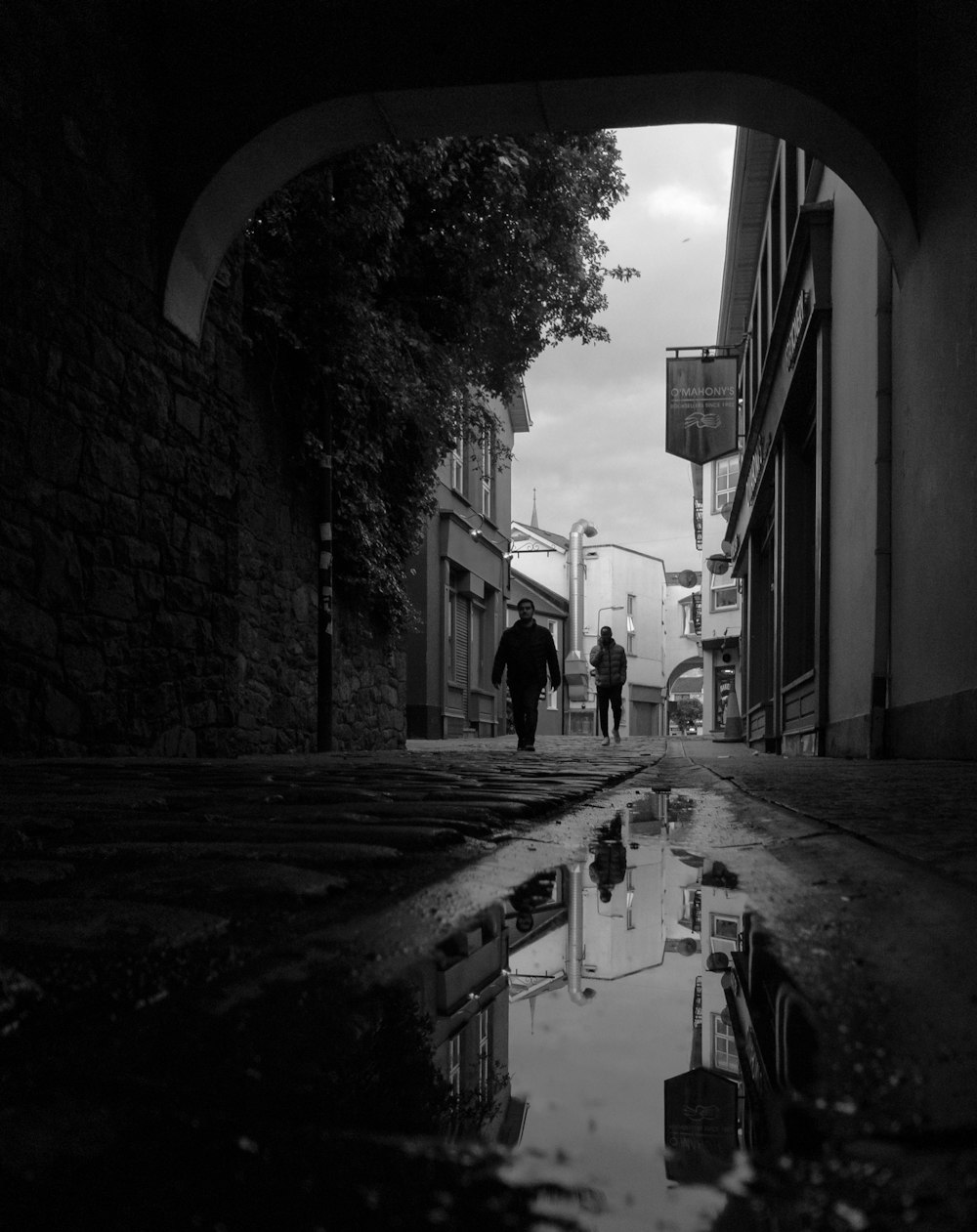 grayscale photo of man walking on sidewalk