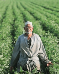 man in gray thobe sitting on green grass during daytime