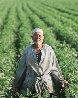 man in gray thobe sitting on green grass during daytime