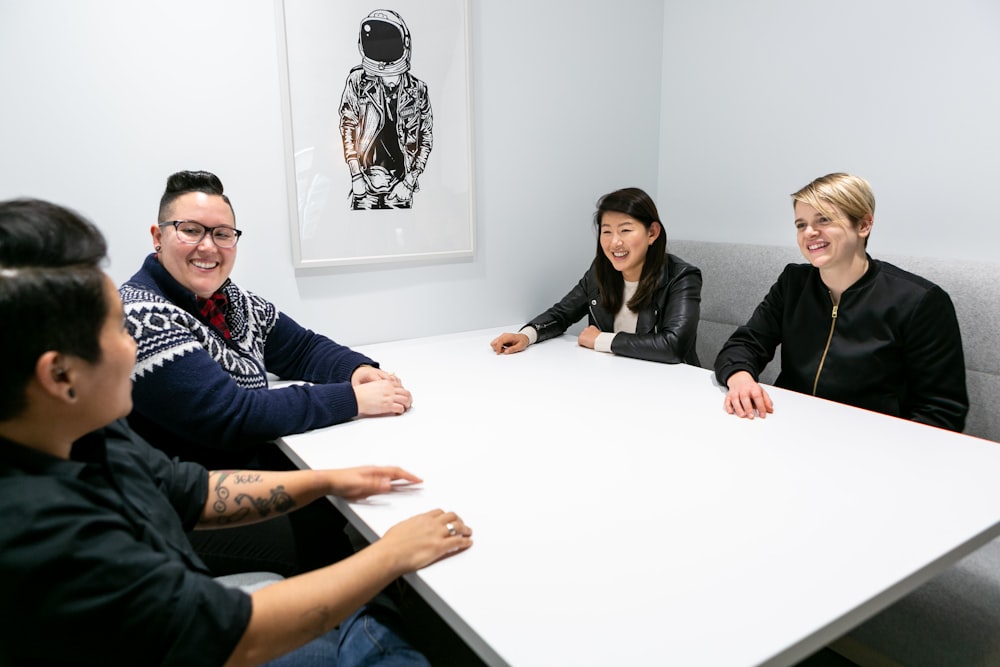 group of four people smiling sitting around white boardroom table