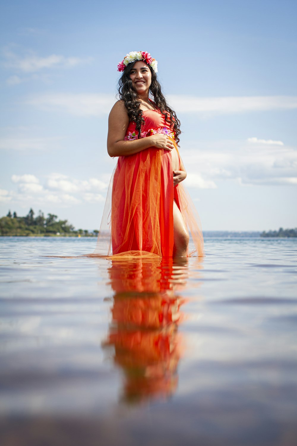 昼間、水の上に立つオレンジ色のノースリーブのドレスを着た女性