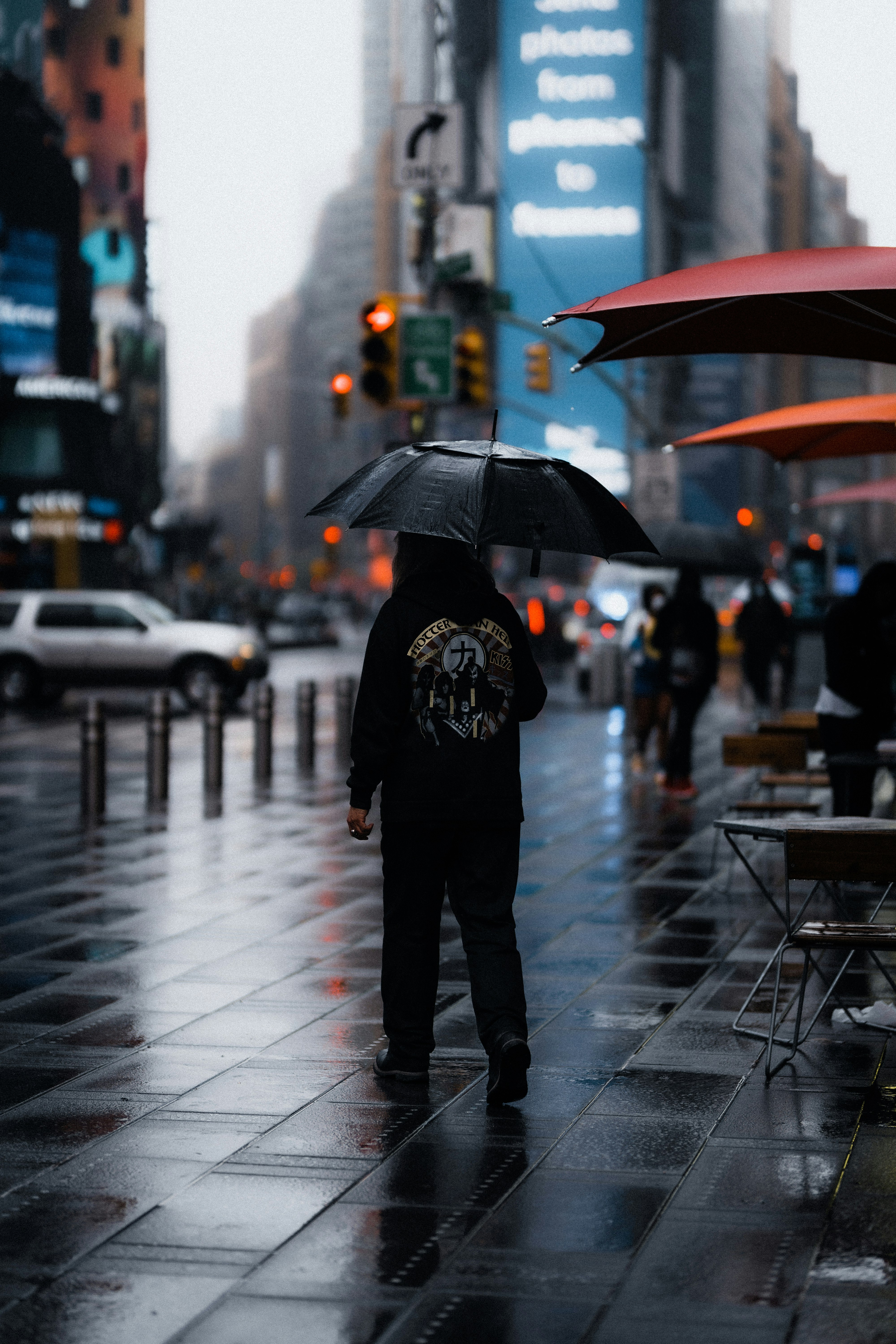 man in black jacket and pants holding umbrella walking on sidewalk during daytime