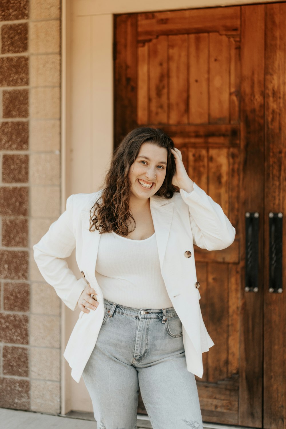 woman in white long sleeve shirt and blue denim jeans standing near brown wooden door