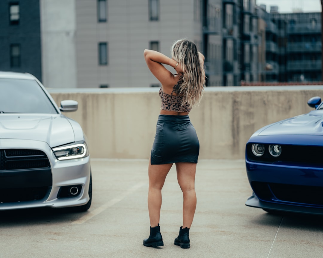 woman in black mini dress standing beside blue bmw car during daytime