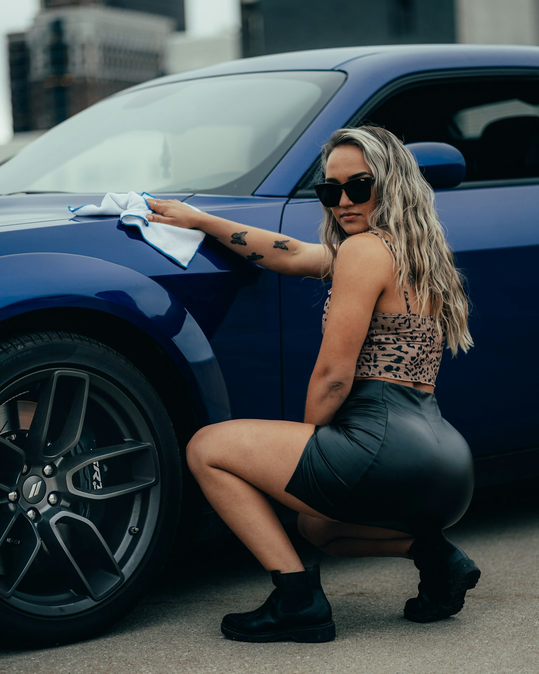 woman in yellow tank top and black skirt leaning on blue car