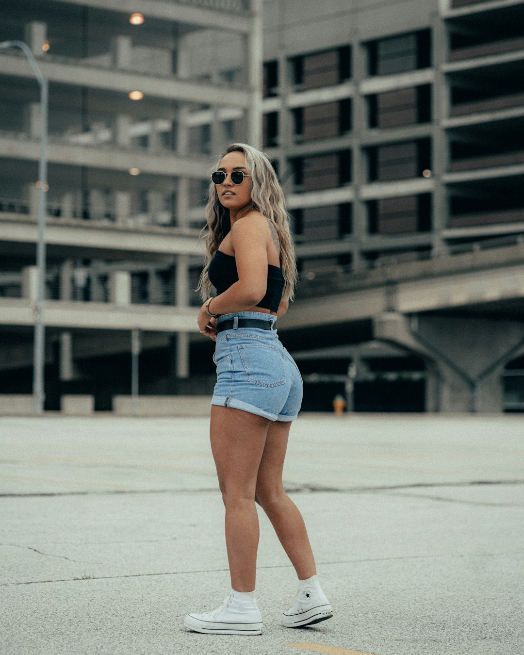woman in blue denim shorts and white sunglasses standing on white concrete floor during daytime