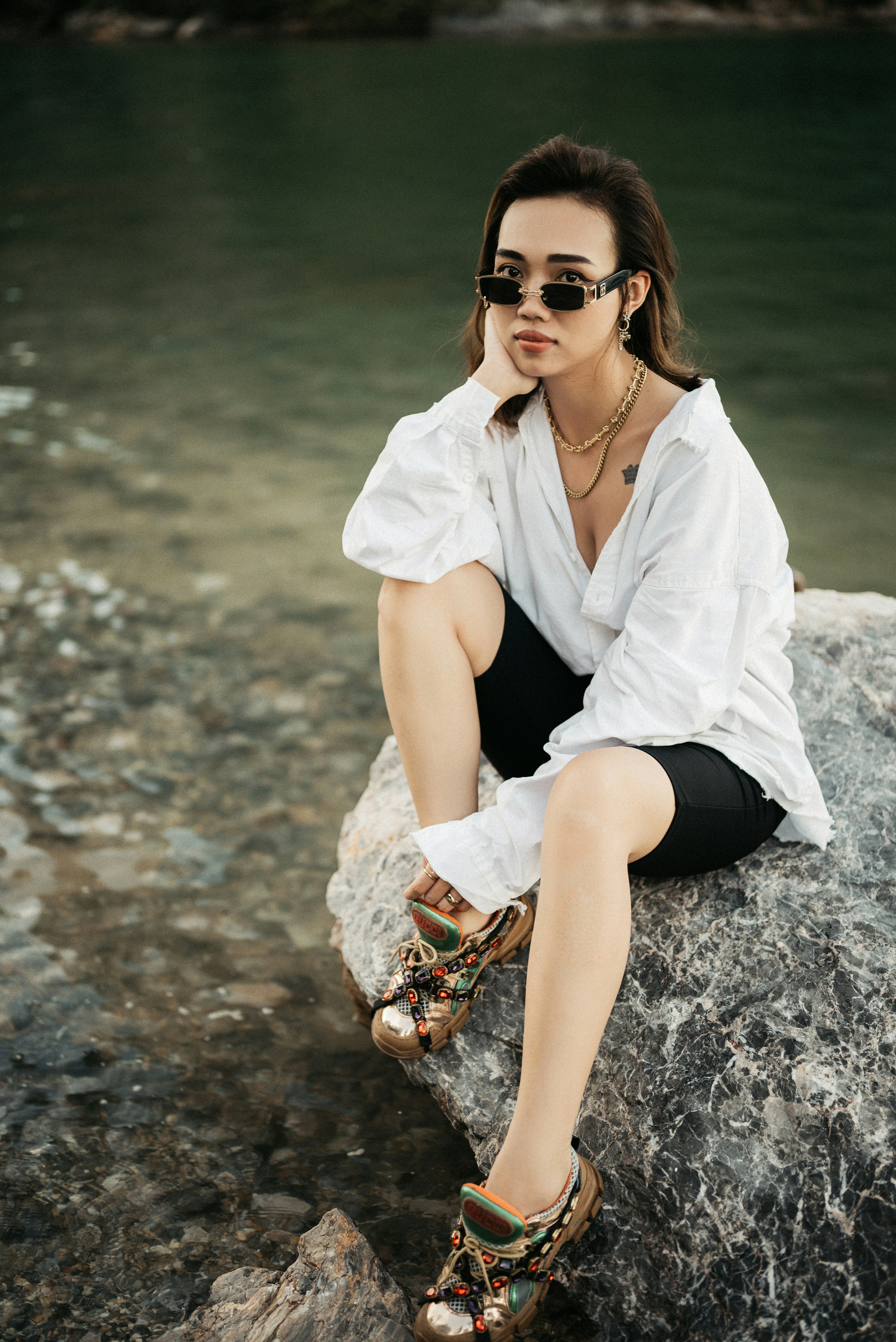 woman in white button up shirt and black shorts sitting on white sand during daytime