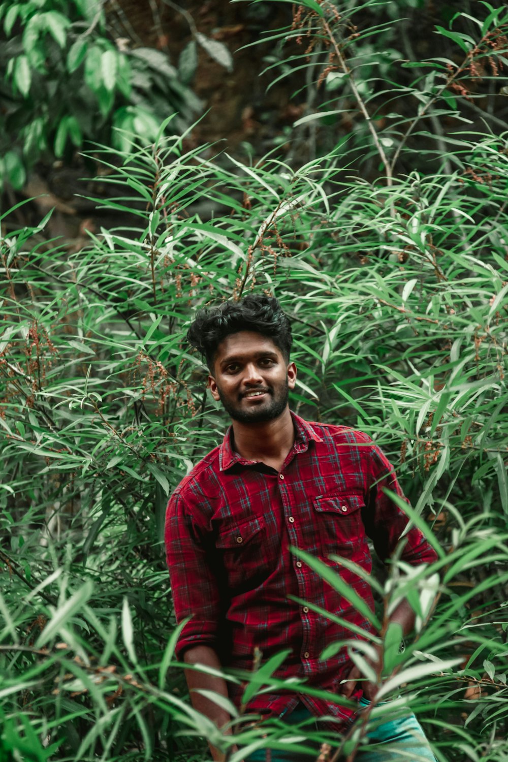 man in red and white plaid dress shirt standing near green plants during daytime