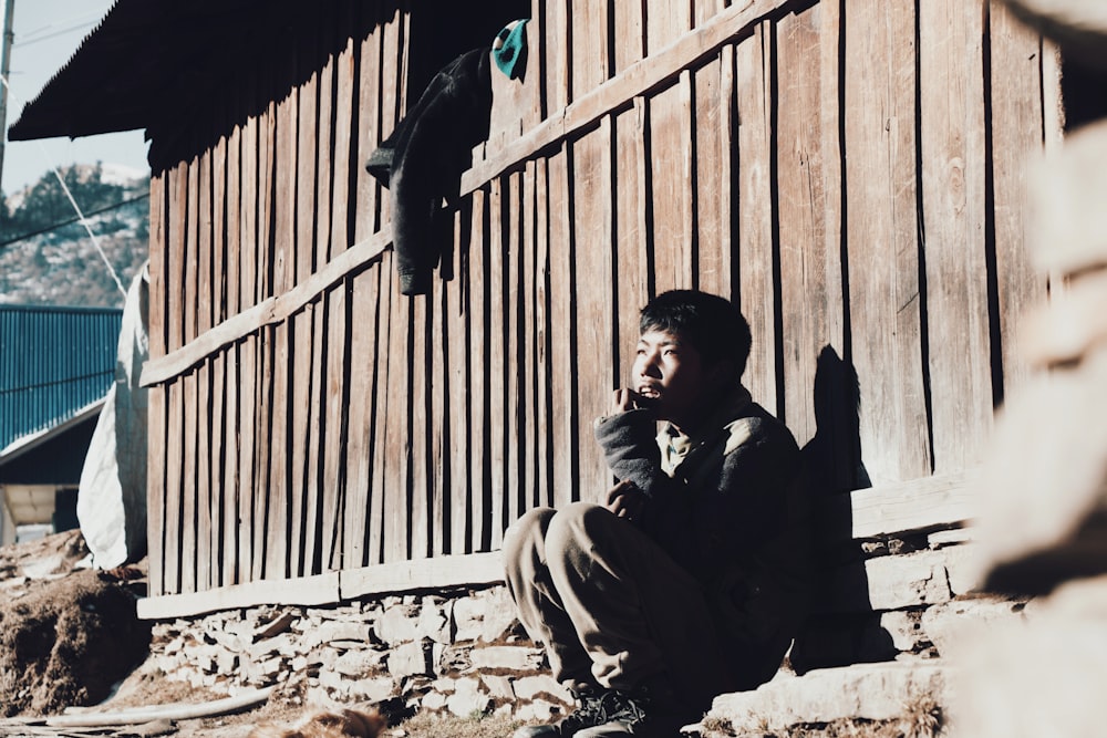 man in black jacket sitting on brown concrete stairs