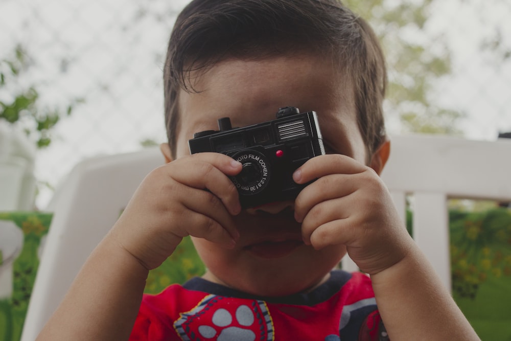 Junge in rot-blauem Rundhals-T-Shirt mit schwarzer DSLR-Kamera