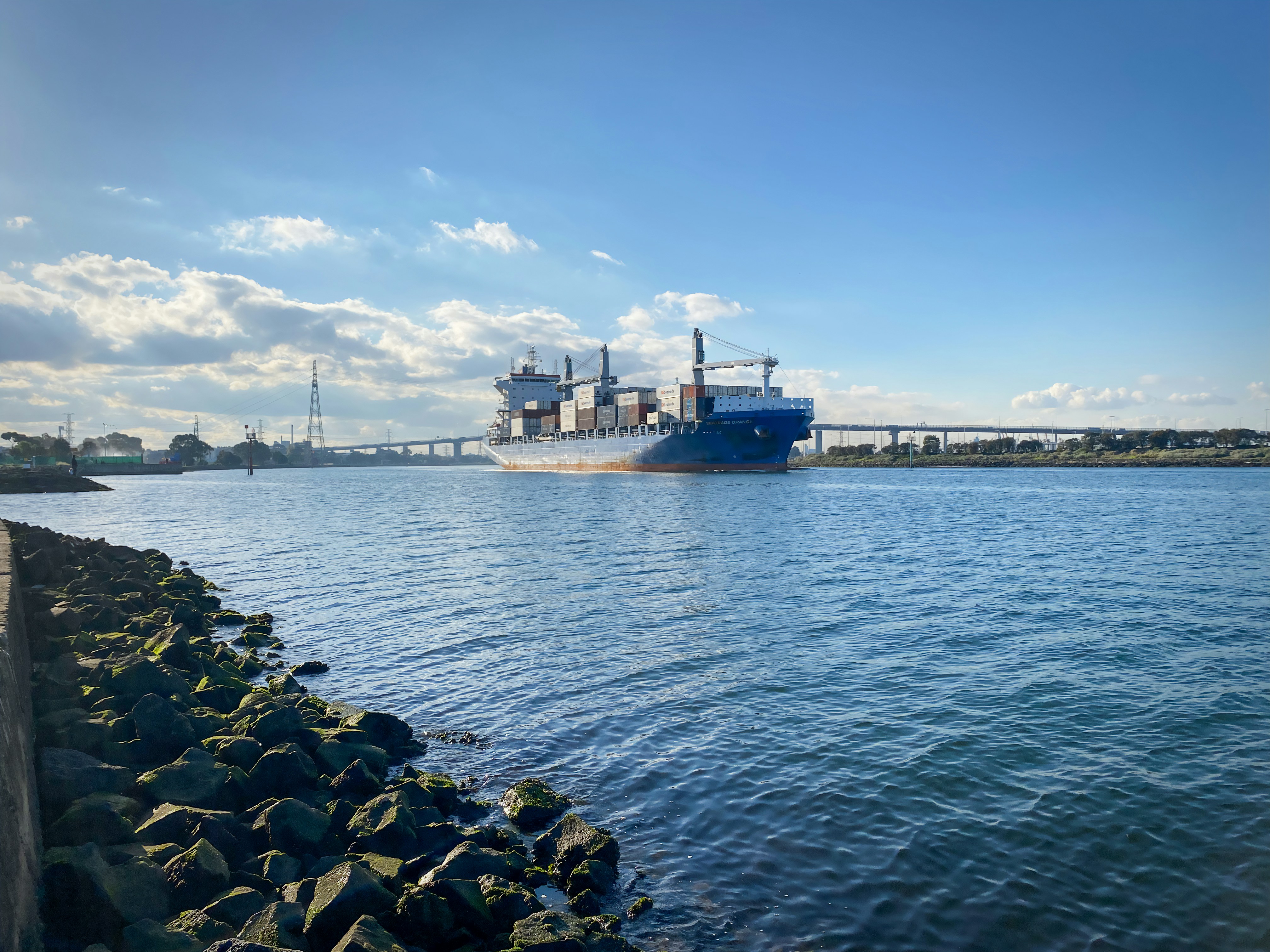 Cargo ship full of containers sails under a bright blue sky.