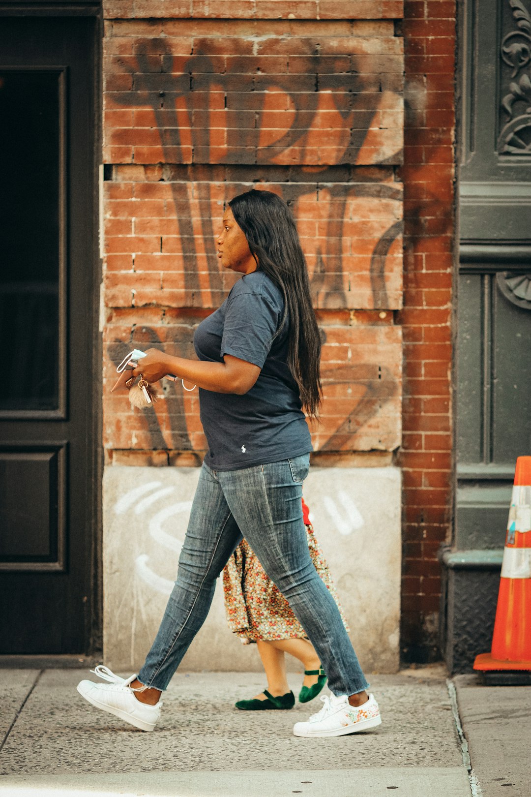 woman in gray t-shirt and blue denim jeans standing in front of brown brick wall