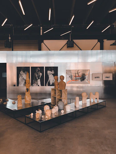 Gallery wall showcasing a mix of modern paintings and stone sculptures under soft lighting.