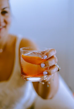 A moody close-up shot of a hand holding a classic amber cocktail against the backdrop of exposed brick and warm candlelight.