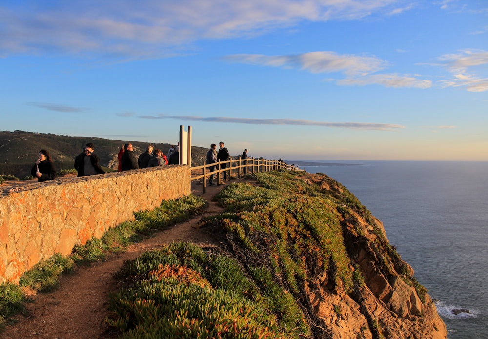 people standing on brown rock formation near sea under blue sky during daytime