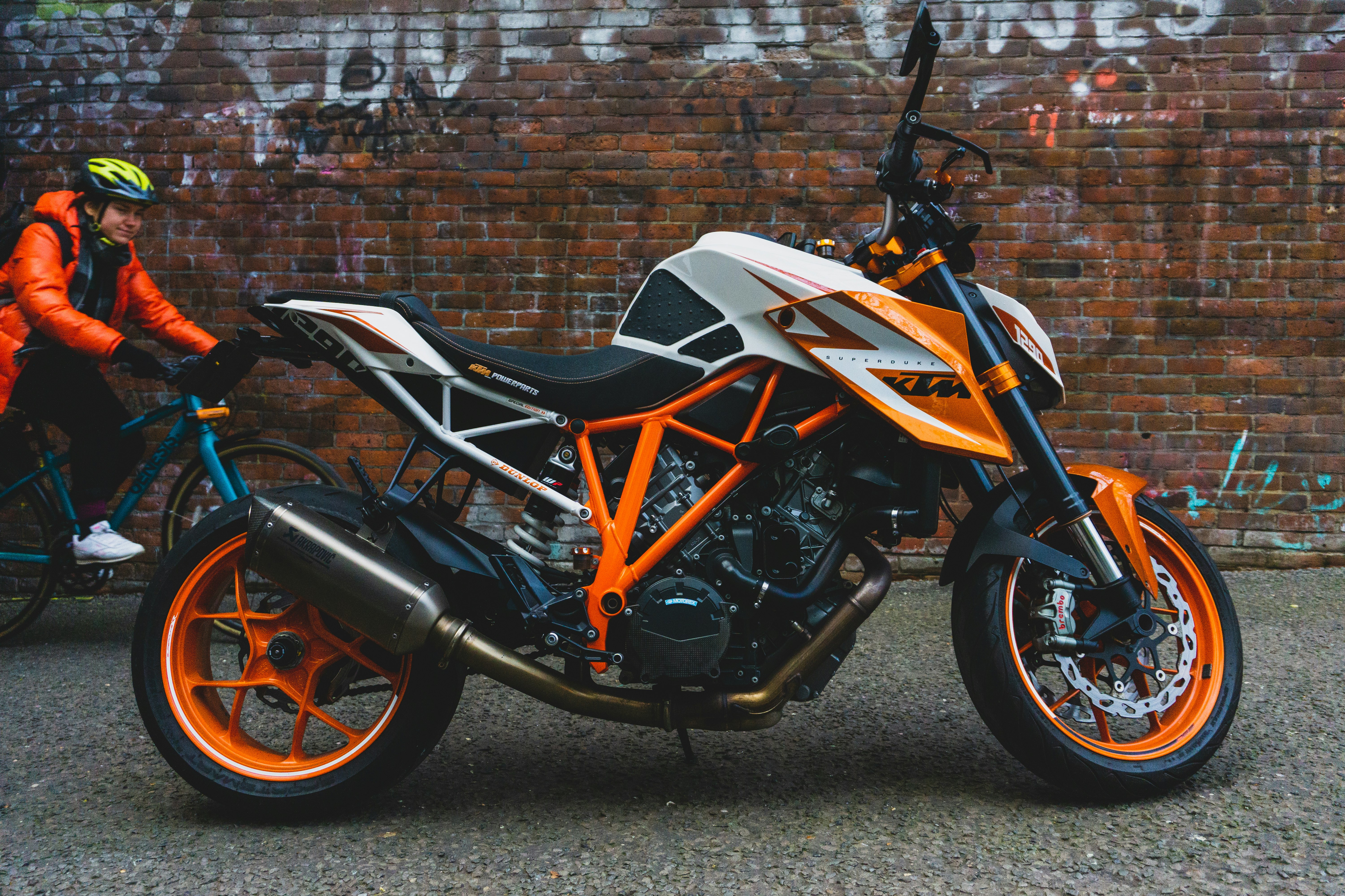 black and orange motorcycle parked beside brown brick wall