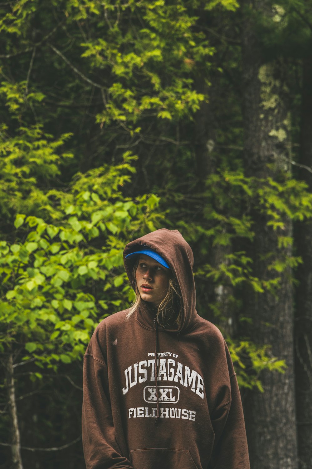 man in brown and white hoodie standing near green trees during daytime