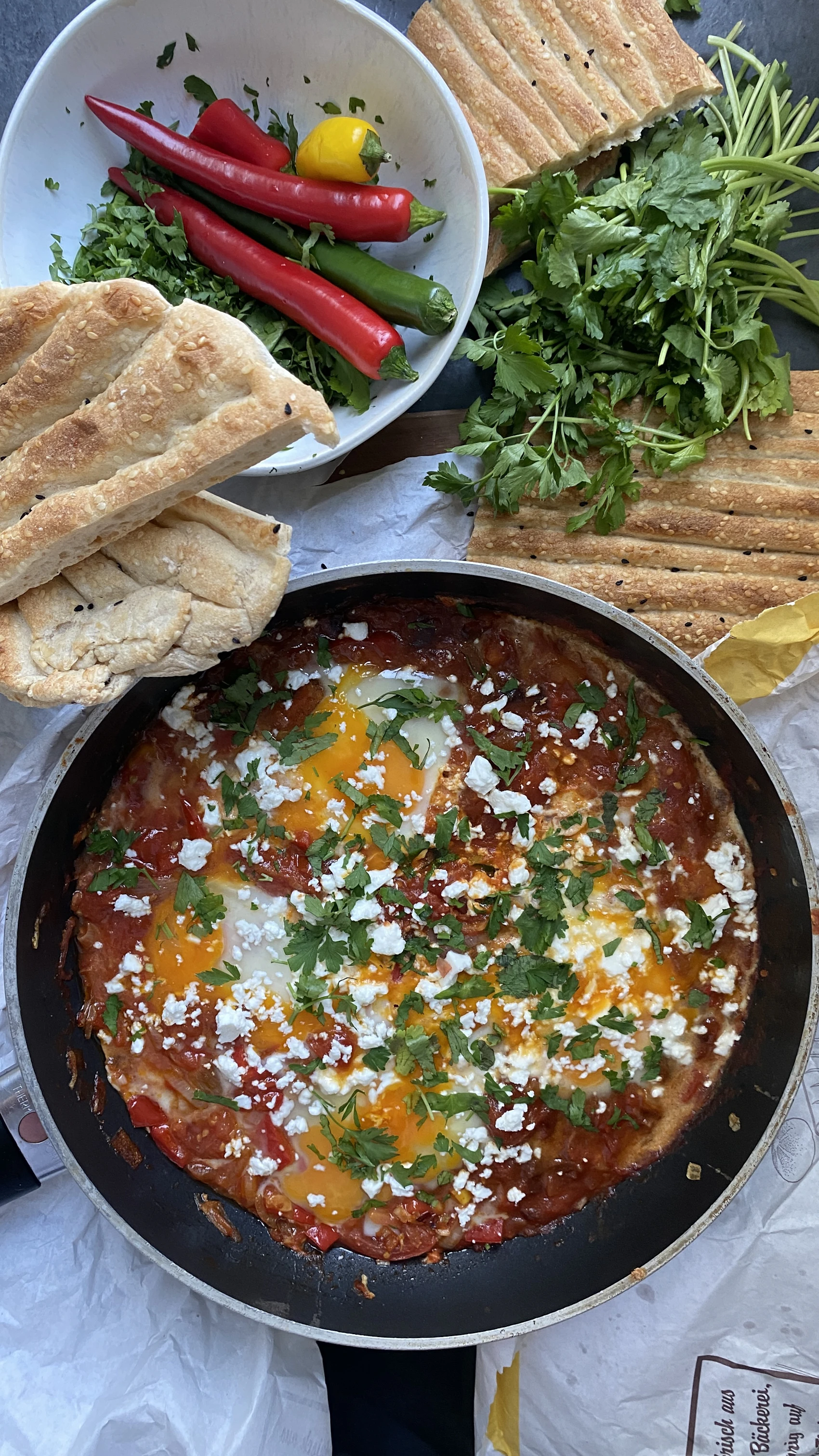 Freshly baked Levantine flatbread beside a sizzling pan of shakshuka with herbs and feta.