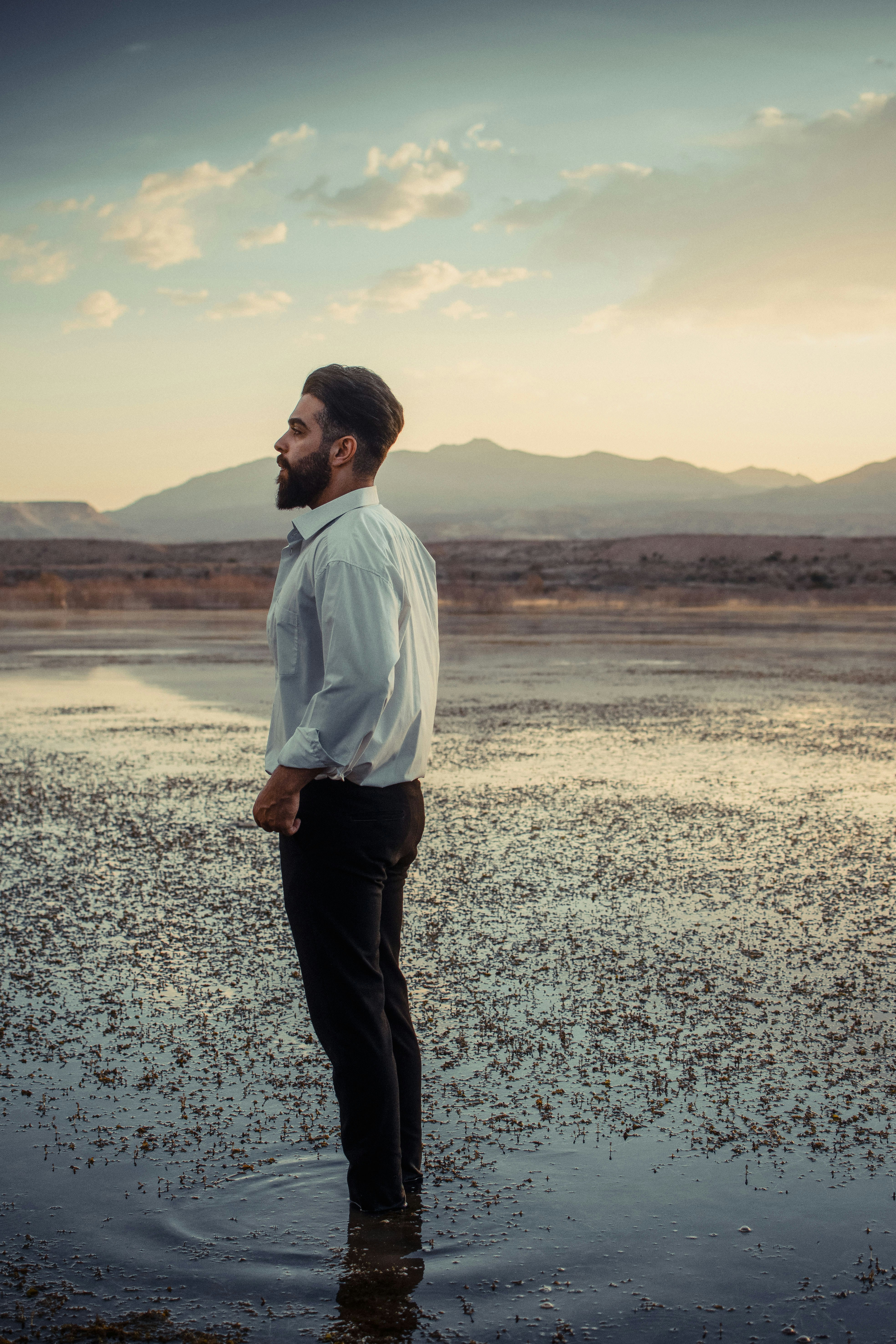 man in white dress shirt and black pants standing on gray sand during daytime